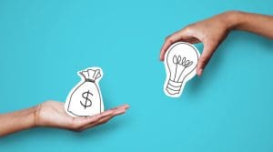 Two hands against a blue background: one holds a paper cutout of a money bag with a dollar sign, and the other holds a lightbulb, representing exchanging money for ideas—highlighting Online Reputation Management costs.