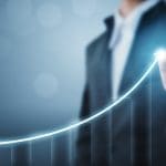 A person in a suit points to the peak of a glowing, upward-trending line graph. The background is blurred, emphasizing the graph that symbolizes growth or success. This visual underscores the importance of corporate reputation management and suggests positive progress in business or data metrics.