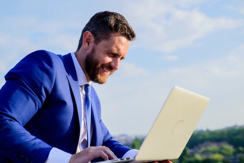 A CEO in a suit is using a laptop for CEO reputation management.