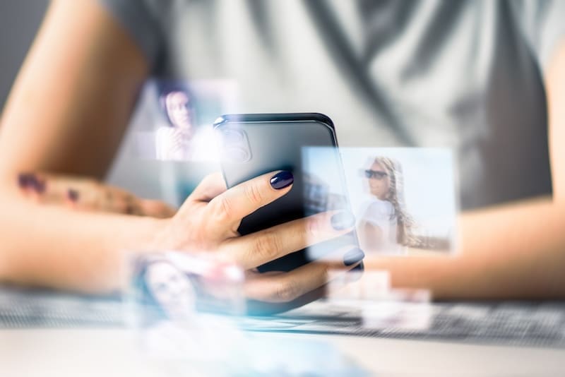 A person holding a smartphone with floating, semi-transparent images of people around the device, suggesting digital interaction or even dark web photo search activity.