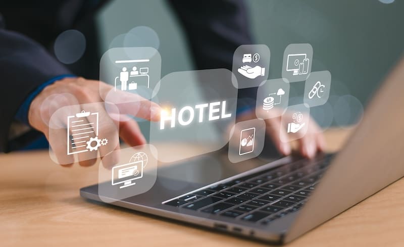 A person in a suit uses a laptop with floating icons representing hotel services—booking, check-in, concierge, food, and payment—showcasing digital hotel management, online reservations, and modern hotel reputation management.