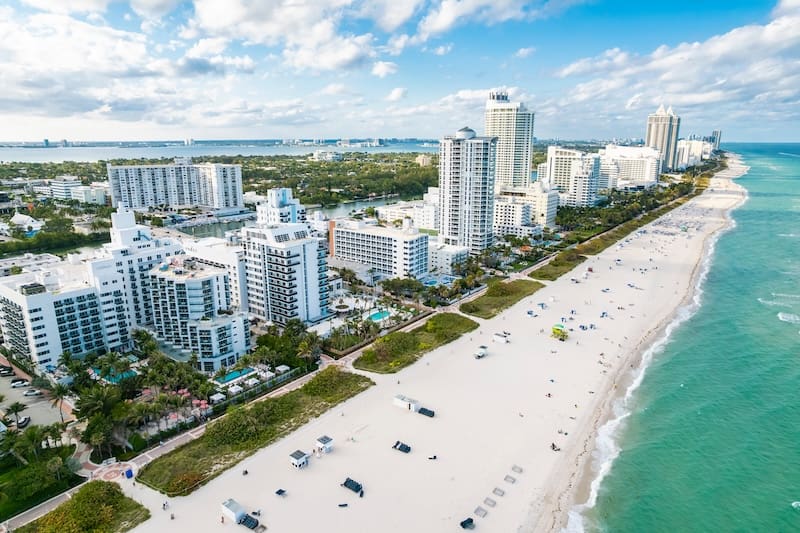 Aerial view of a beach lined with white sand and turquoise water, with numerous high-rise hotels—renowned for their hotel reputation management—stretching along the shoreline under a partly cloudy sky.