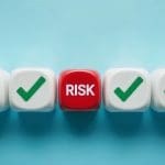 A row of white cubes with green check marks surrounds a single red cube in the center labeled "RISK," all set against a light blue background.