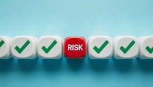 A row of white cubes with green check marks surrounds a single red cube in the center labeled "RISK," all set against a light blue background.