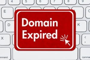 A red sign with white text reading "Domain Expired" and a mouse cursor icon is placed on a white computer keyboard.