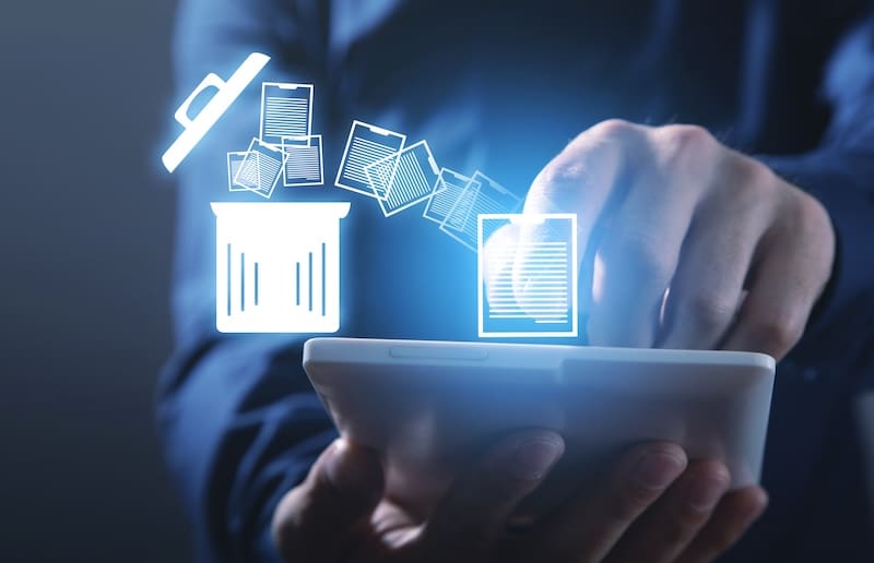 A person uses a tablet, with digital icons showing files being moved into a trash bin, symbolizing deleting or removing files electronically, such as when you remove court records from PlainSite.