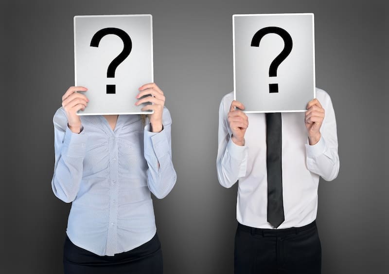 Two people stand side by side, each holding a sign with a large question mark that hides their identity—like those seeking to remove court records from PlainSite. One wears a blouse, the other a dress shirt and tie, against a gray background.