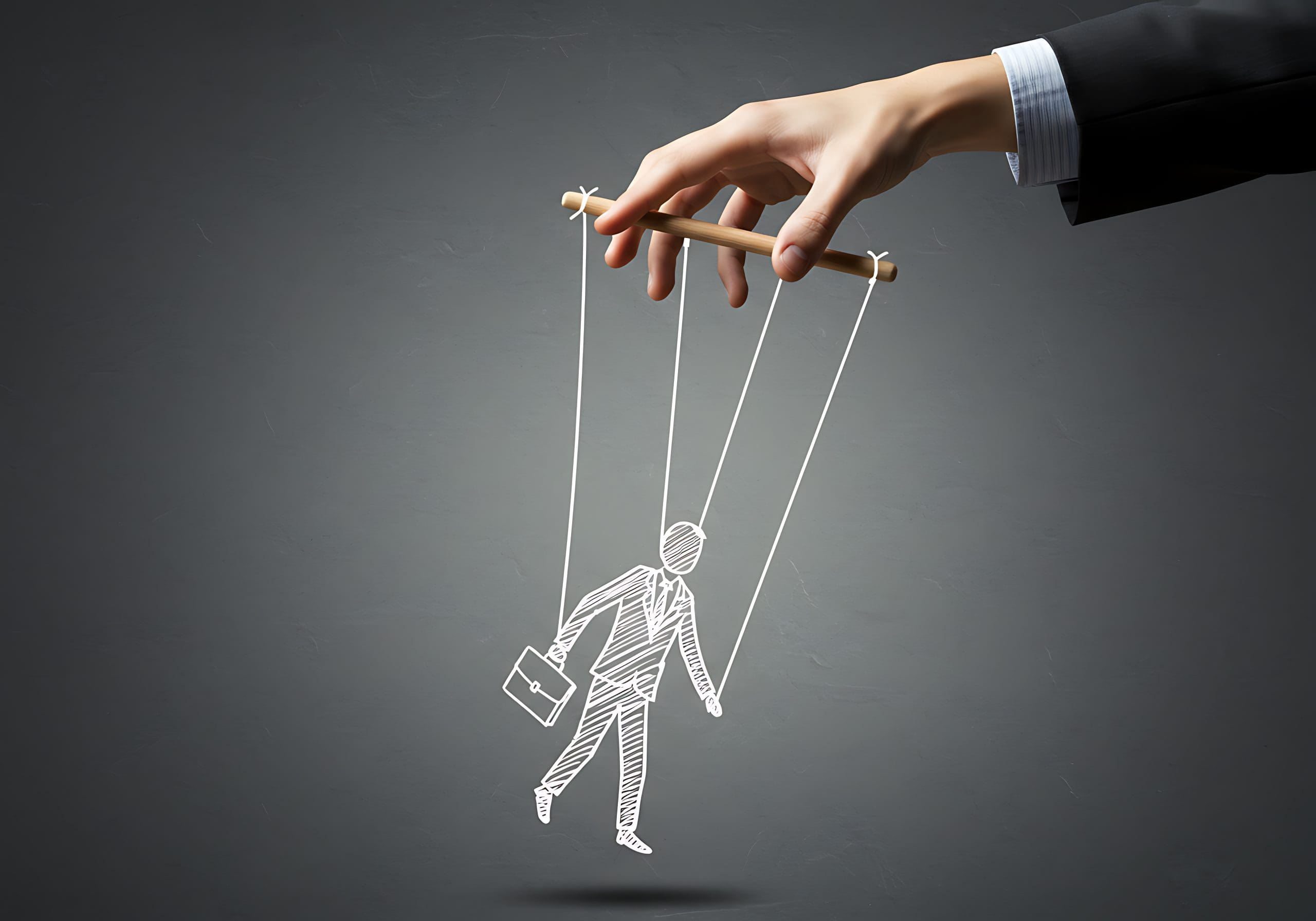 A hand in a suit holds strings attached to a drawn puppet figure of a person carrying a briefcase, symbolizing control or manipulation, against a dark gray background.