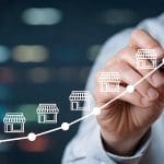 A person in business attire draws an upward-curving graph with storefront icons along the line, symbolizing franchise reputation and business growth. The blurred background suggests an office or corporate environment.