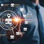 A man in a suit touches a virtual screen displaying a network of small store icons connected around a central store, with star ratings beside each icon representing franchise review management for multiple business locations.